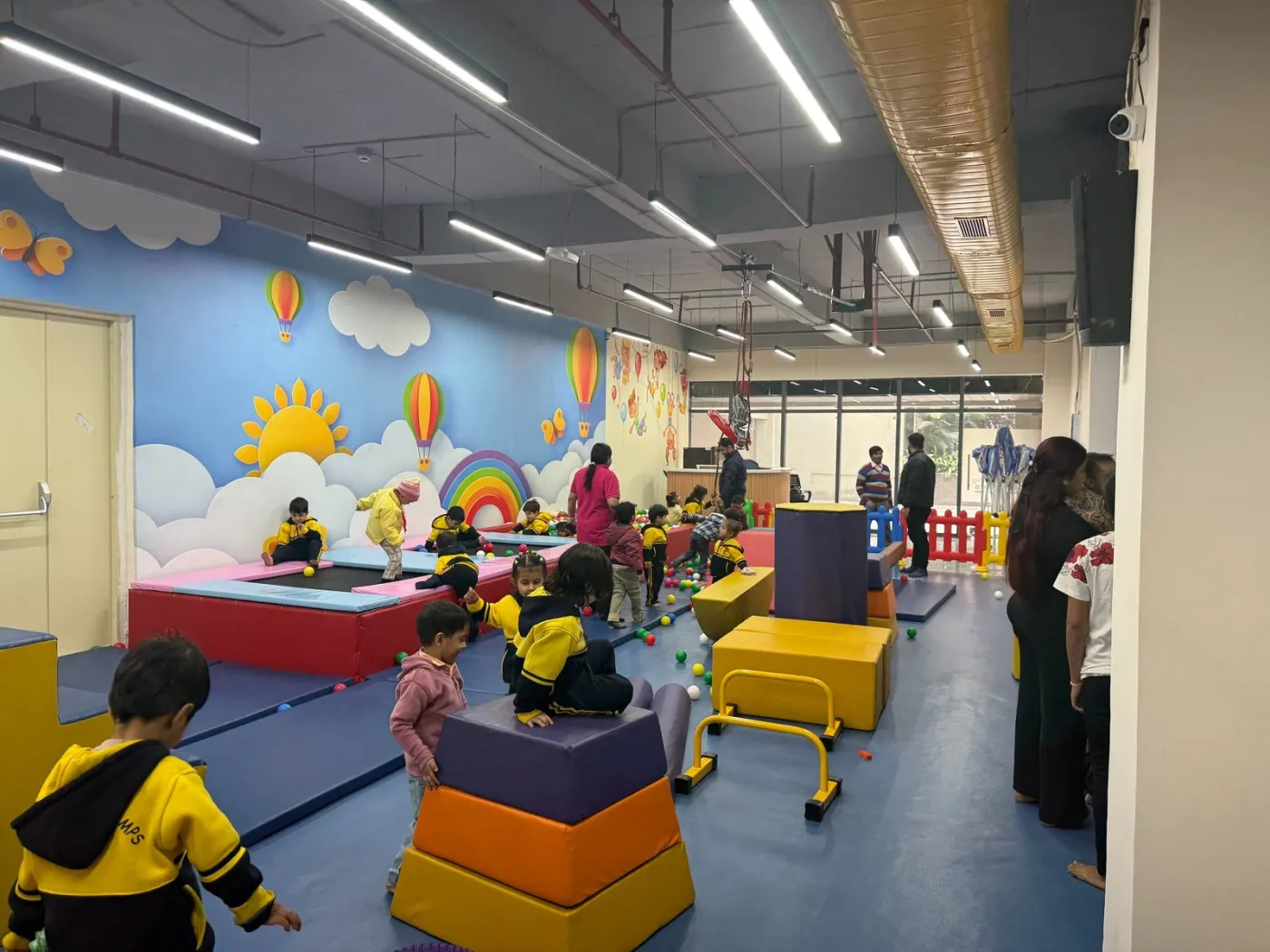 Children playing across the wide activity floor of a kids' gym
